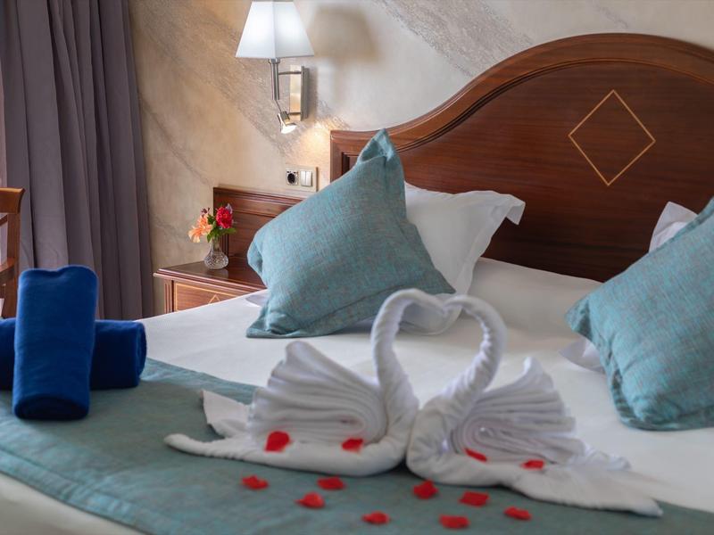 Lit d'hôtel décoré avec des serviettes en forme de cygnes et des pétales de rose rouges