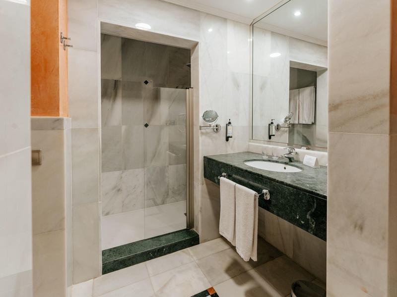 Salle de bain lumineuse avec grande douche, lavabo et serviettes.