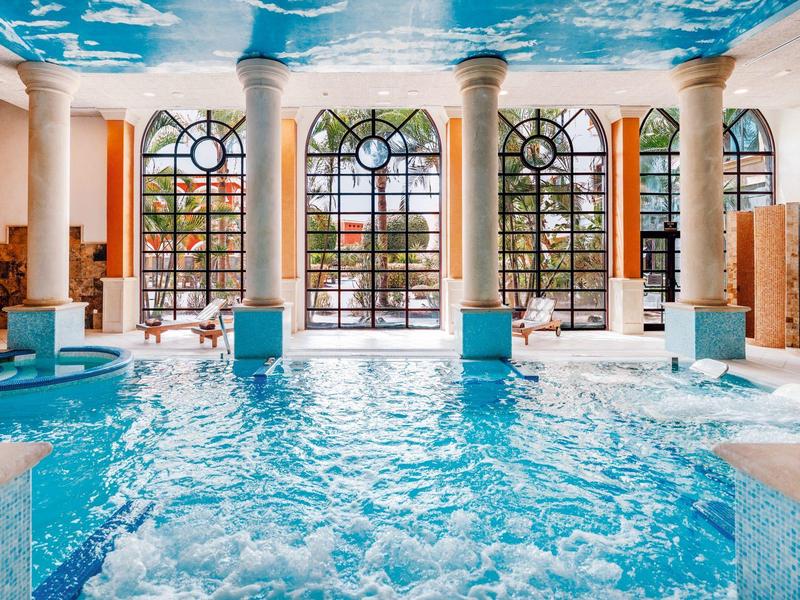 Piscine intérieure lumineuse avec carreaux bleus, colonnes et grandes fenêtres cintrées