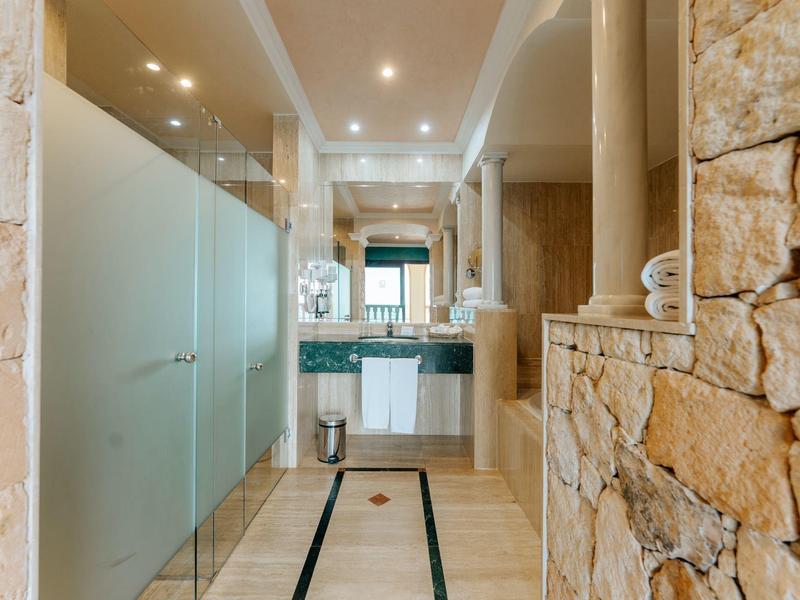 Salle de bain lumineuse avec mur en pierre naturelle, douche à l'italienne et double vasque.