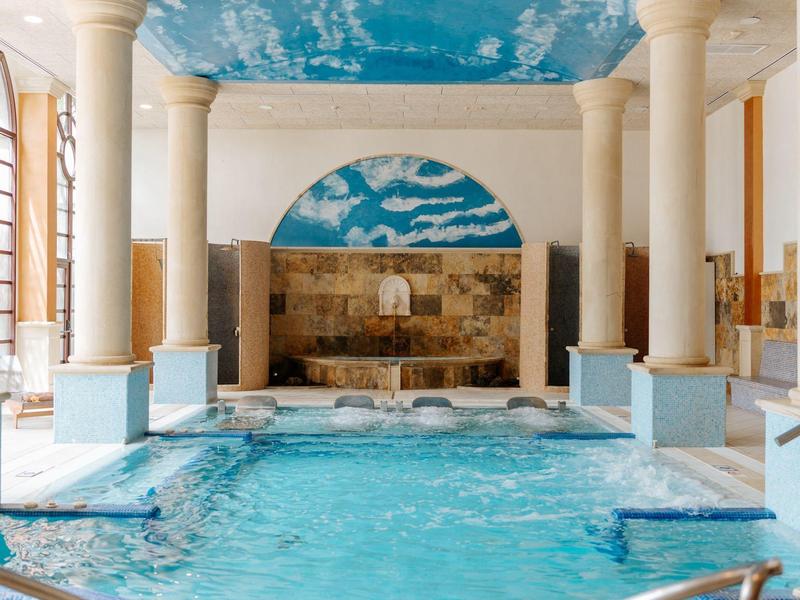 Piscine intérieure avec colonnes et plafond bleu ciel dans un espace spa élégant.
