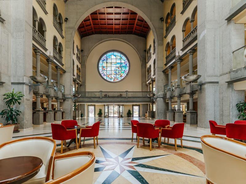 Hall d'hôtel élégant avec fauteuils rouges, sol en marbre et grande fenêtre ronde en vitrail.