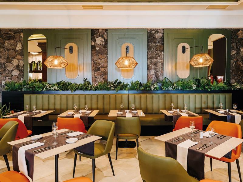 Intérieur de restaurant moderne avec des chaises colorées, des tables en bois et des lampes murales décoratives.