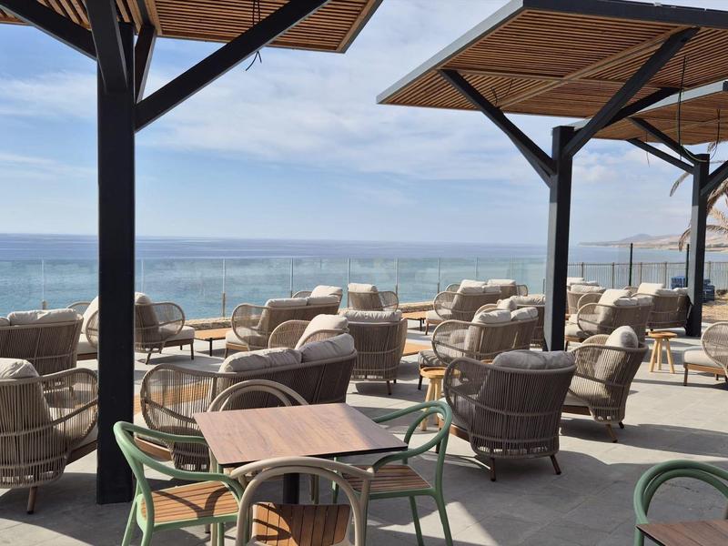 Terrasse avec des chaises et des tables confortables face à la mer sous un ciel clair.