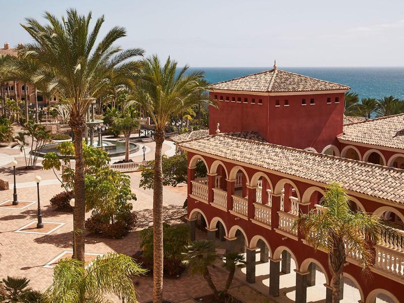 Complexe de bâtiments rouges à côté de palmiers avec vue sur la mer sous un ciel clair.