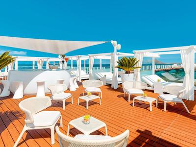 Zonnig buitenterras met witte stoelen, tafels en potplanten met uitzicht op zee.