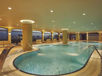 Grande piscina coperta di lusso con colonne illuminate e getti d'acqua rilassanti.