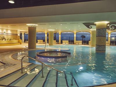 Overdekt hotelzwembad met ronde jacuzzi en panoramische ramen met uitzicht op zee.