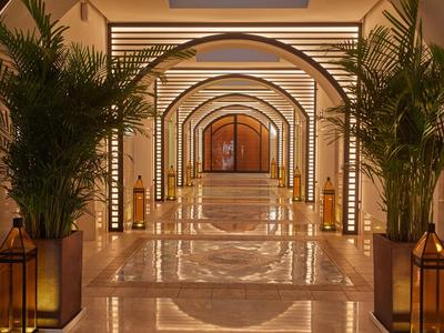 Luxe hotelgang met bogen, marmeren vloer en grote groene planten in lantaarns.