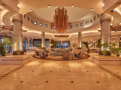 Ampio ed elegante hall dell'hotel con aree salotto circolari, colonne e illuminazione calda.