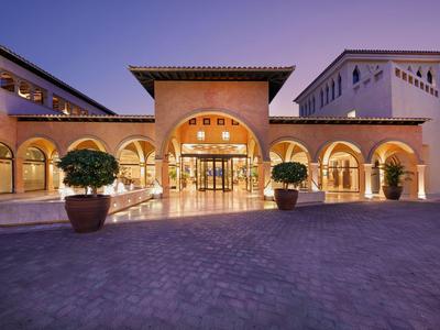 Ingresso dell'hotel illuminato con archi e piante in vaso al crepuscolo.