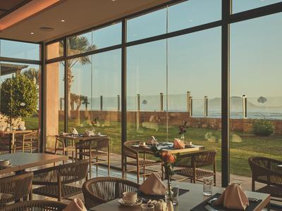 Ristorante luminoso con grandi finestre di vetro che si affacciano sul giardino e sul mare.