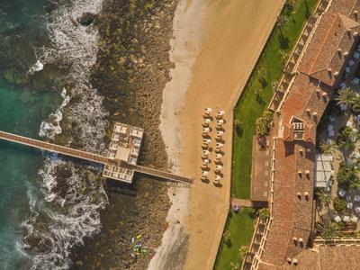 Luchtfoto van een kustresort met een pier die de zee in loopt en ligstoelen op het zandstrand.