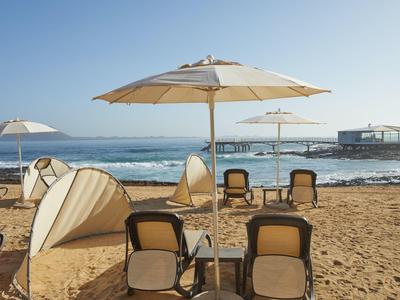 Strand met parasols en ligstoelen gericht op de oceaan onder een heldere blauwe lucht.