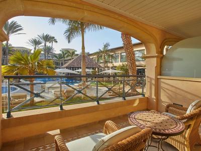 Balkon met uitzicht op een zwembad met palmbomen en ligstoelen bij een resort.