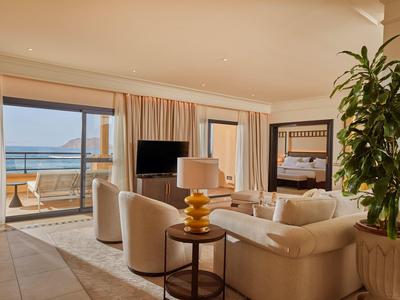 Gezellige woonkamer met beige banken, een tv en een grote plant, met uitzicht op het balkon aan zee.