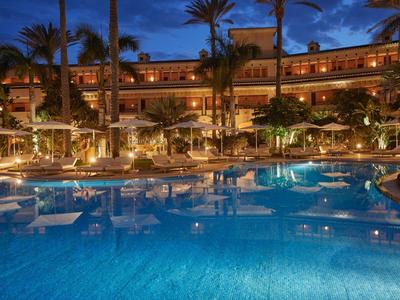 Nachtzicht op resortzwembad met verlicht hotel en palmbomen op de achtergrond