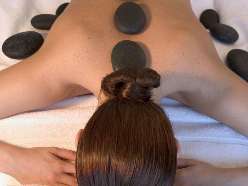 Persoon ontvangt hotstone massage liggend op buik met stenen op rug en armen.