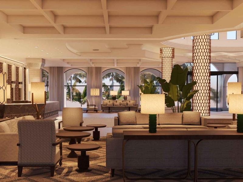 Ruime hotel lobby met beige banken, fauteuils en moderne lampen op houten tafels.