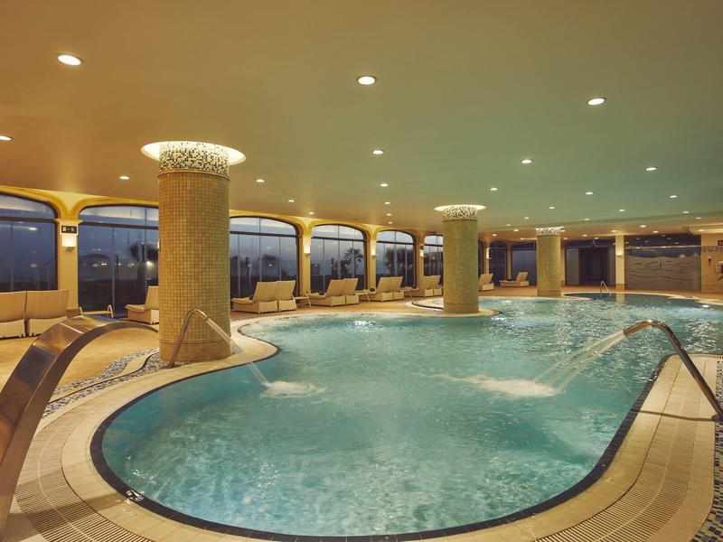 Overdekt zwembad met ligstoelen en warme verlichting.