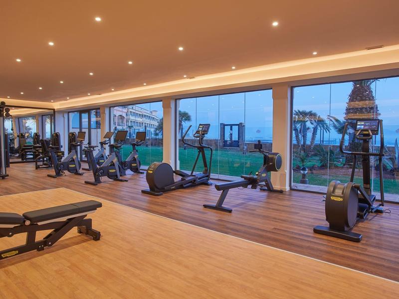 Moderne sportschool met hometrainers en grote ramen met uitzicht op groen bij schemering.