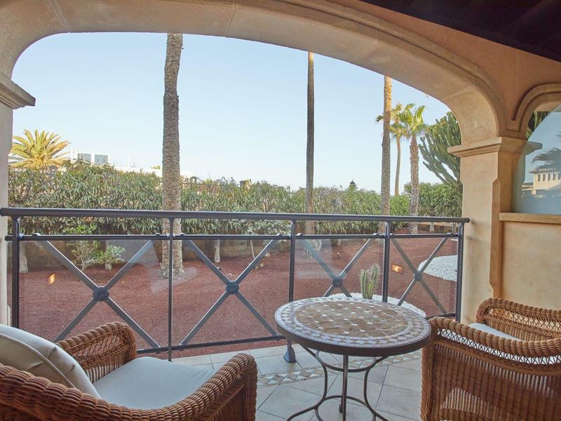 Gezellig balkon met stoelen en tafel met uitzicht op een tuin met palmbomen in zonlicht.