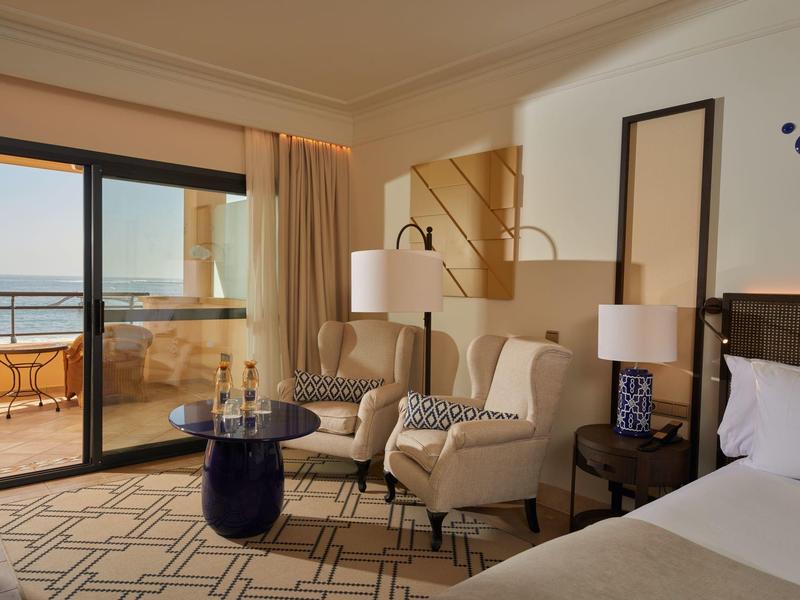 Gezellige hotelkamer met stoelen, een kleine tafel en zeezicht door schuifdeuren.