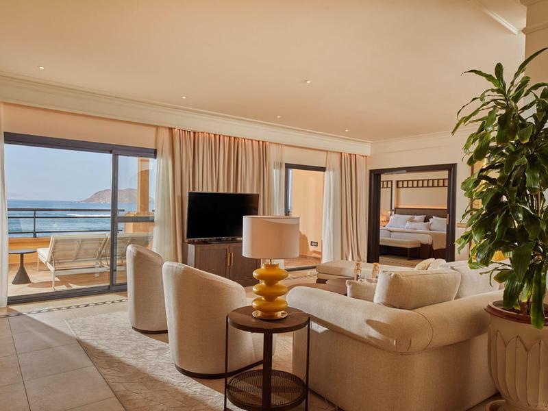 Gezellige woonkamer met beige banken, een tv en een grote plant, met uitzicht op het balkon aan zee.