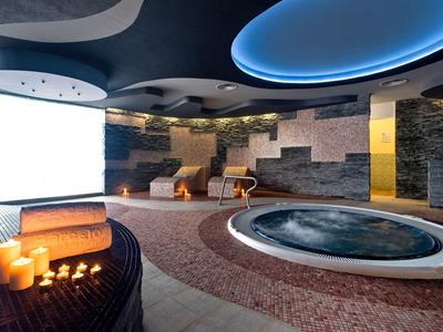 Nowoczesne spa z jacuzzi, zapalonymi świecami i drewnianymi leżakami.