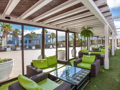 Covered outdoor terrace with green chairs and sofas at a hotel.