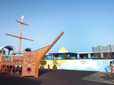 Plac zabaw wodnych na świeżym powietrzu z dużym drewnianym statkiem i bawiącymi się dziećmi.