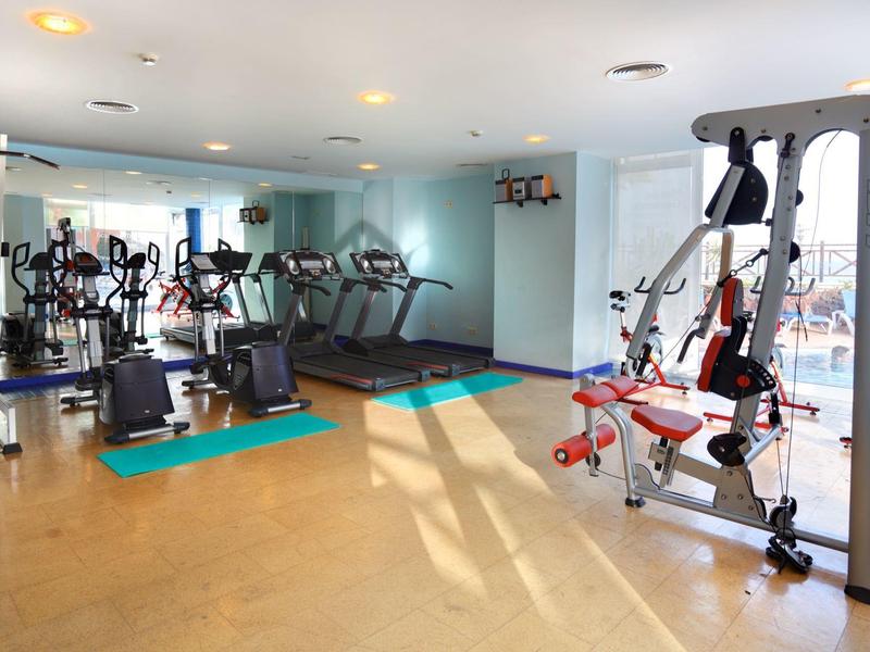 Nowoczesna siłownia z różnorodnym sprzętem i dużymi oknami wpuszczającymi światło.