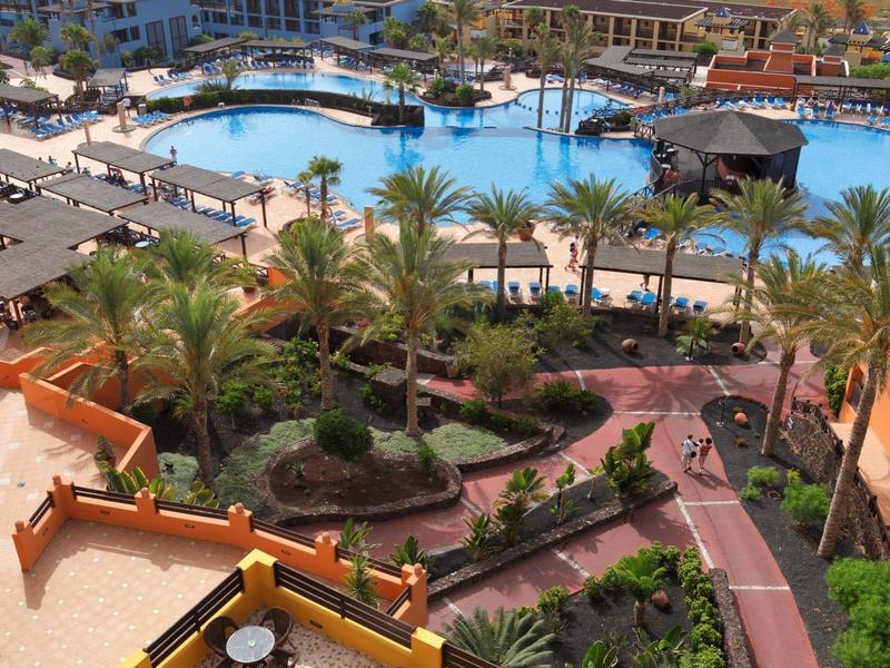 Basen z tarasami, palmami i widokiem na plażę oraz morze na horyzoncie.