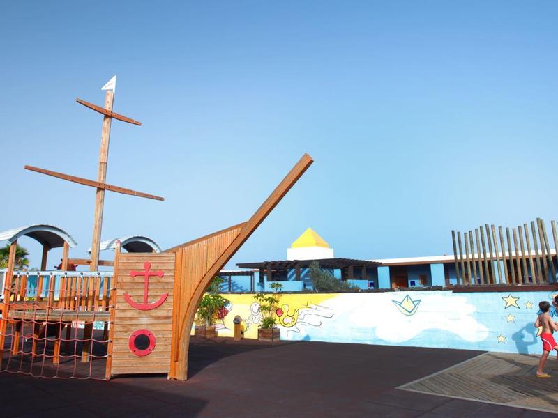 Plac zabaw wodnych na świeżym powietrzu z dużym drewnianym statkiem i bawiącymi się dziećmi.