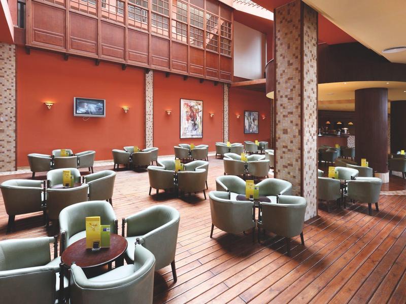 Przestronny salon hotelowy z zielonymi fotelami i drewnianą podłogą.