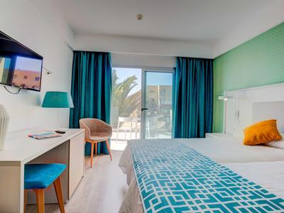 Nowoczesny pokój hotelowy z łóżkiem podwójnym, biurkiem, krzesłami i balkonem z widokiem na palmy.