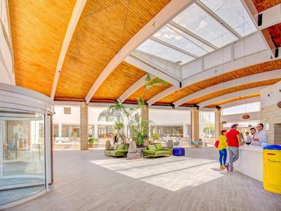 Luminosa hall d'hotel con archi in legno, piante e persone vicino all'ingresso.