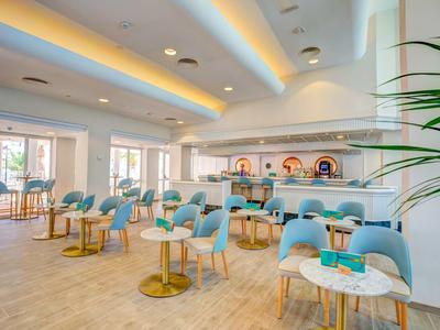 Jasny, nowoczesny bar hotelowy z niebieskimi krzesłami i białymi stołami w eleganckim otoczeniu.