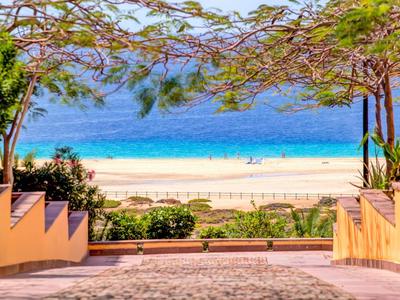 Vista dal giardino dell'hotel sulla spiaggia e sul mare azzurro sotto un cielo sereno.