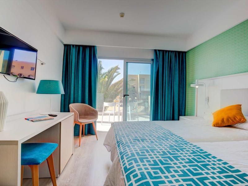 Camera d'hotel moderna con letto matrimoniale, tende blu e scrivania con sedia.