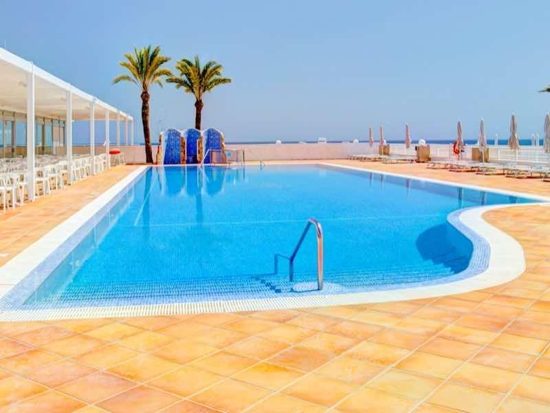 Piscina esterna moderna con lettini e vista mare in una giornata di sole.