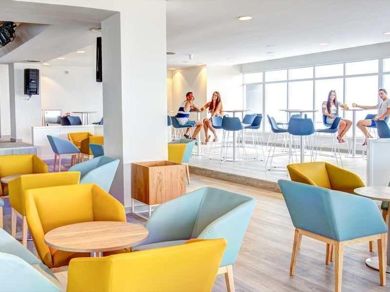 Ristorante luminoso e moderno con sedie colorate e grandi finestre con vista sul mare.