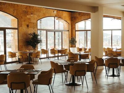 Jasna kawiarnia z stołami, krzesłami i dużymi oknami w ciepłej atmosferze.