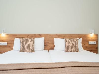 Dwa pojedyncze łóżka z drewnianym zagłówkiem i beżowymi poduszkami dekoracyjnymi.