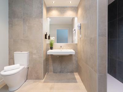 Nowoczesna łazienka z beżowymi płytkami, podwieszana umywalka i toaleta.