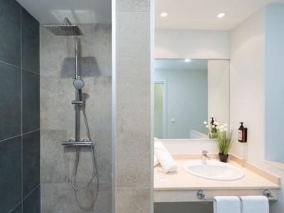 Nowoczesny prysznic po lewej, umywalka i lustro po prawej w jasnej łazience.