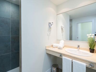 Helles Badezimmer mit großem Spiegel, Waschbecken, Handtüchern und begehbarer Dusche mit dunklen Fliesen.