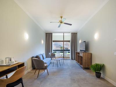 Nowoczesny salon z fotelami, stołem, telewizorem i balkonem z widokiem, przytulna atmosfera.