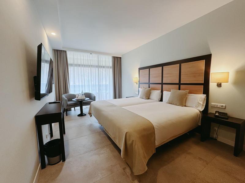 Nowoczesny pokój hotelowy z łóżkiem podwójnym, telewizorem, miejscem do siedzenia i dużymi oknami z zasłonami.