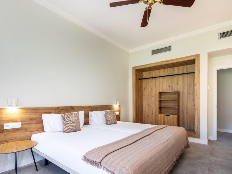 Nowoczesny pokój hotelowy z podwójnym łóżkiem, lampką ścienną i drewnianą szafą.